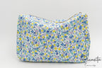 Neceser de tela con flores azules y amarillas visto de frente sobre fondo neutro.