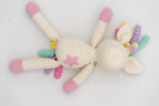 Vista cenital de un unicornio de crochet blanco con patas rosas y melena arcoíris.