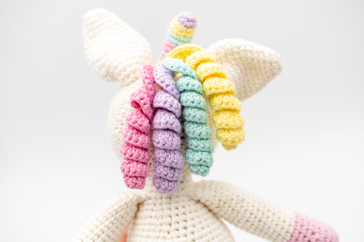 Vista posterior de la cabeza de un unicornio de crochet con rizos de colores pastel.