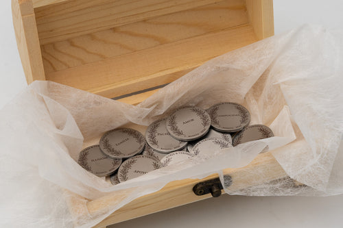 Cofre de madera abierto con arras nupciales envueltas en papel protector blanco.