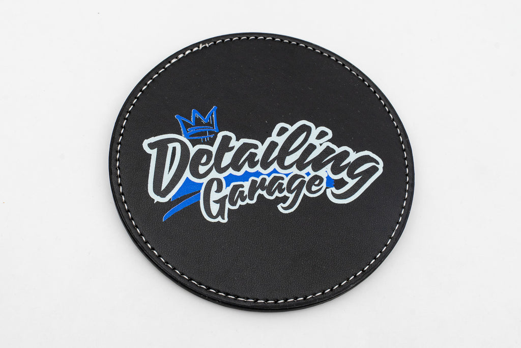 Runder schwarzer Untersetzer mit blauem und gelbem Detailing-Garage-Logo.