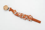 Gerafftes Schnullerband mit Blumen auf terrakottafarbenem Hintergrund und Holzclip