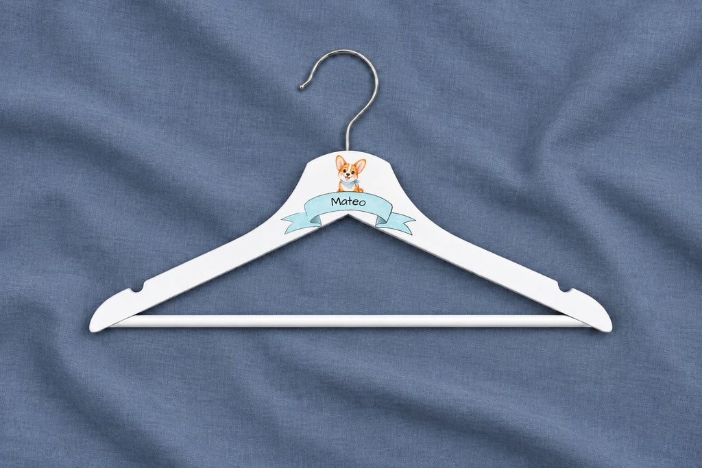 Percha infantil blanca con perrito, cinta azul y nombre Mateo sobre algodón azul liso