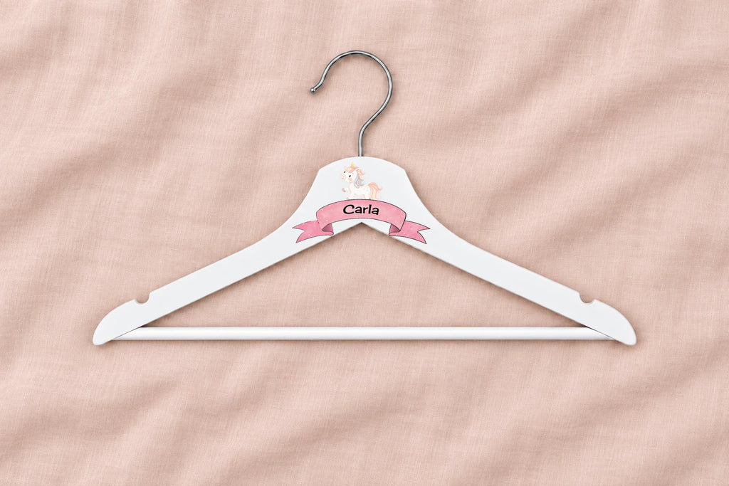 Percha infantil blanca con unicornio, cinta rosa y nombre Carla sobre lino rosa liso
