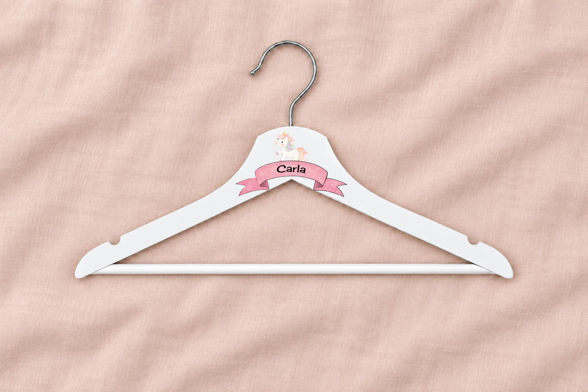 Percha infantil blanca con unicornio, cinta rosa y nombre Carla sobre lino rosa liso
