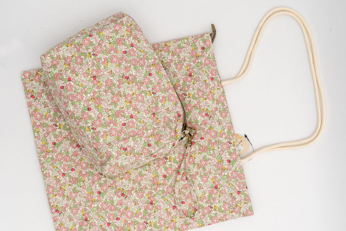 Kosmetiktasche und Baumwollbeutel mit Blumenmuster in Rosa- und Grüntönen auf weißem Hintergrund.