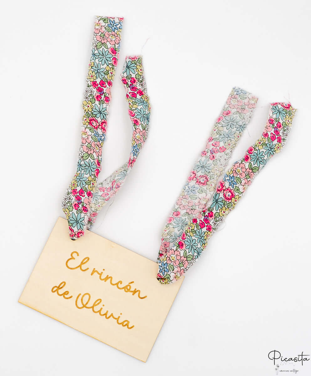 Cartel personalizado de madera Olivia con cintas textiles de flores sobre fondo blanco.