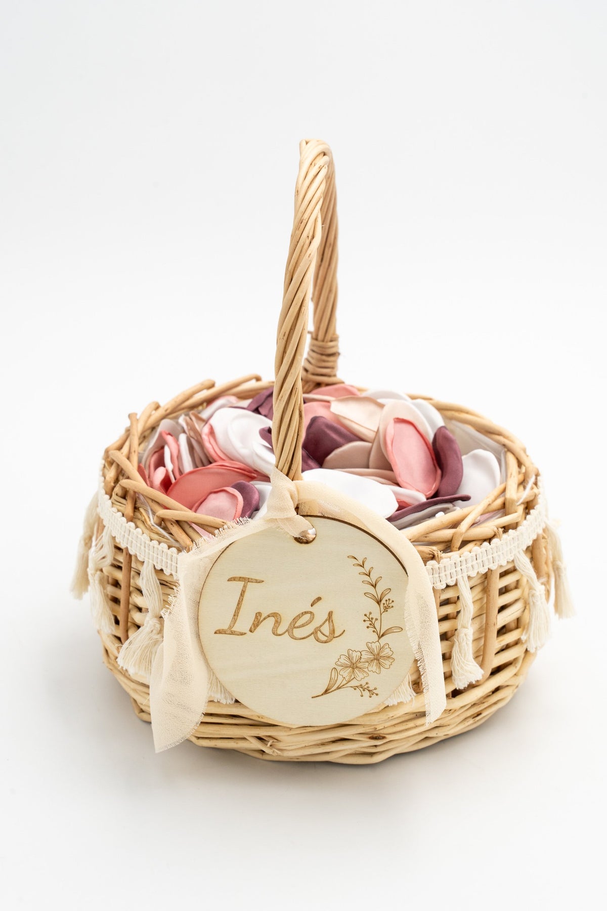 Rattan-Blumenkorb mit weißen Quasten und Stoffblütenblättern in Rosa- und Weißtönen.