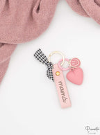 Detalle de la tira de polipiel rosa con grabado mamá y lazo de tela a cuadros.