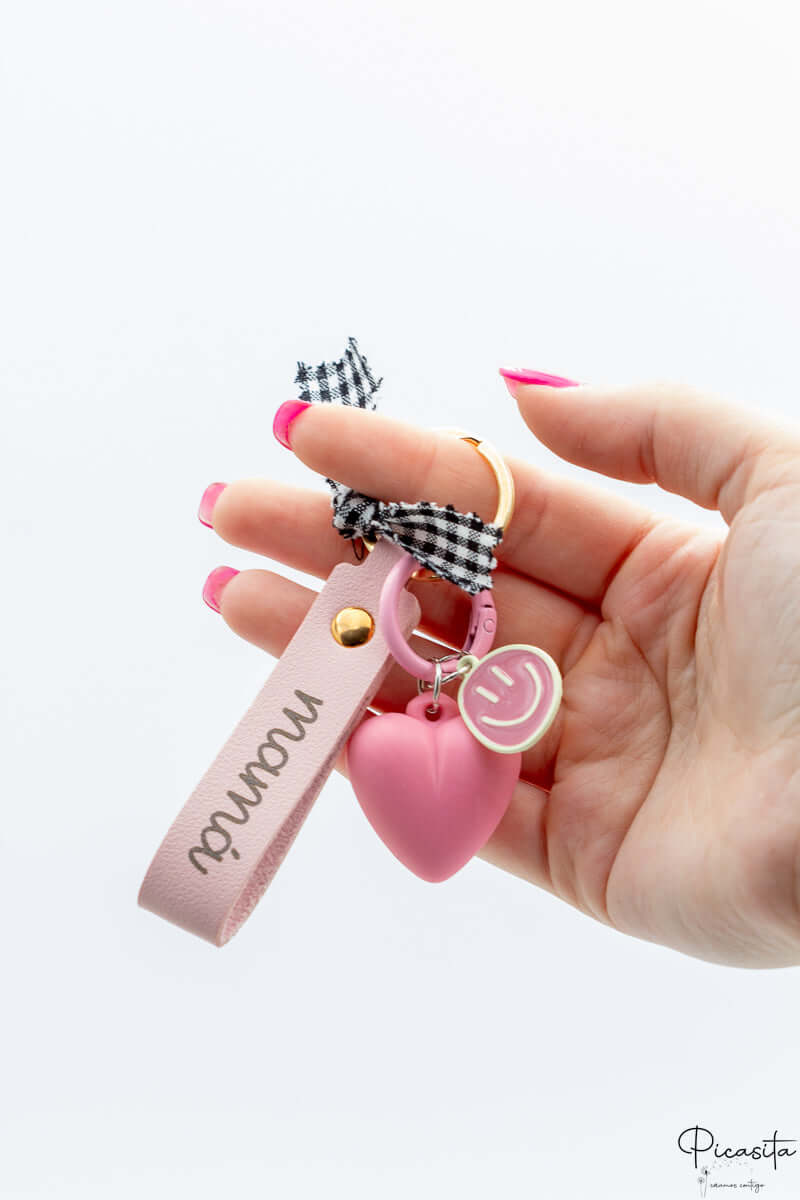 Mano sujetando llavero personalizado rosa con nombre grabado y colgante de corazón de silicona.