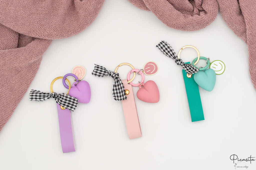 Tres llaveros personalizados en colores púrpura, rosa y aguamarina con charms y anillas doradas.