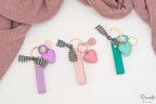 Tres llaveros personalizados en colores púrpura, rosa y aguamarina con charms y anillas doradas.