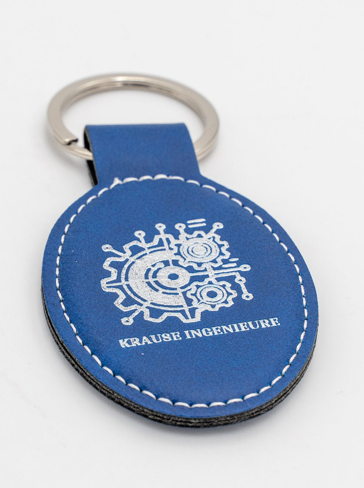 Ovaler blauer Schlüsselanhänger mit hellem Logo und weißer Naht.