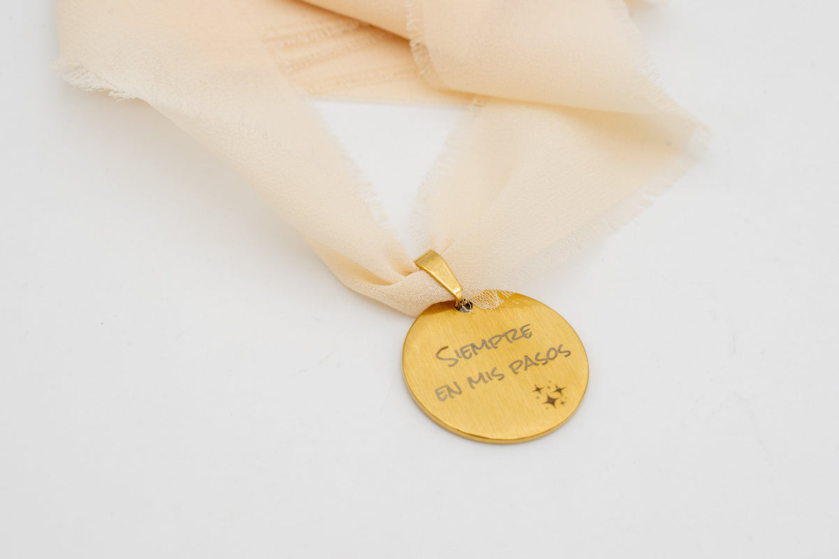 Goldener Anhänger mit dem Spruch „Immer bei meinen Schritten“ an einem pfirsichfarbenen Chiffonband