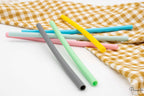 Pajitas de silicona rectas en colores gris, verde y azul sobre superficie blanca.