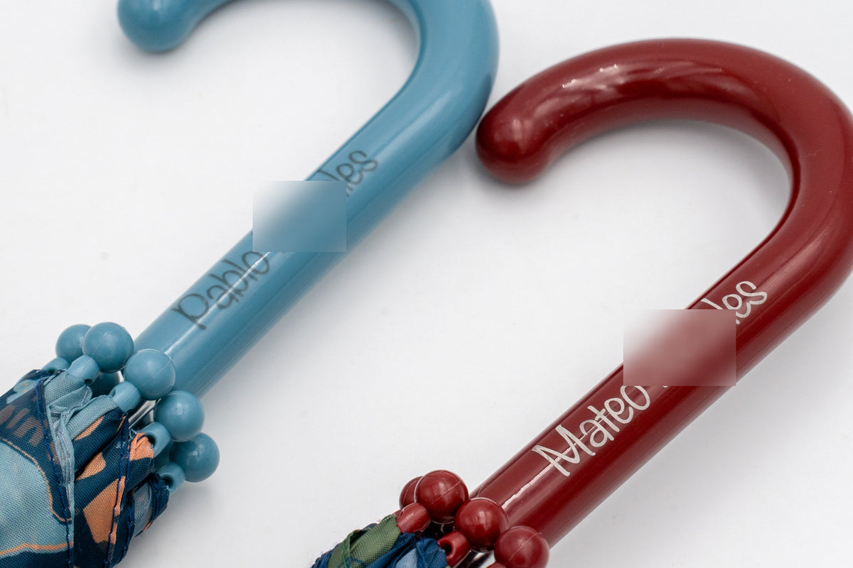 Griffe von Kinderregenschirmen in Blau und Bordeaux mit aufgedruckten Kindernamen