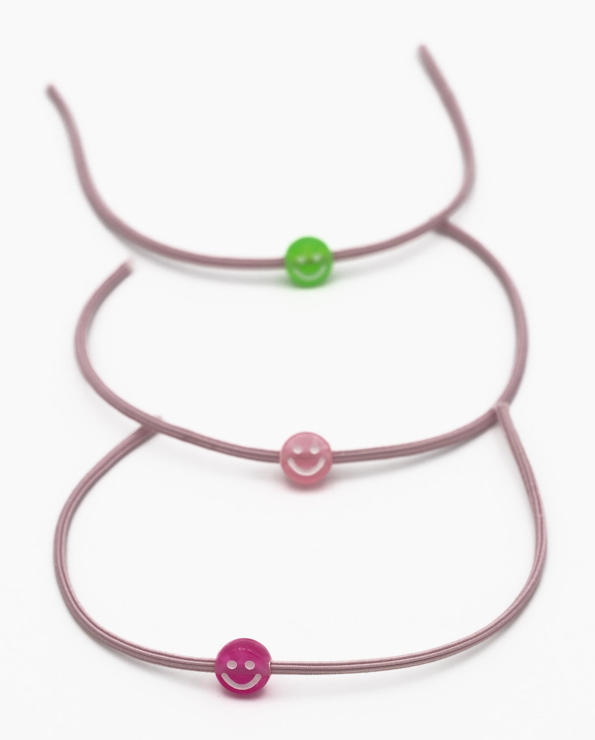 Drei elastische malvenfarbene Armbänder mit grünen und rosa Smiley-Silikonperlen