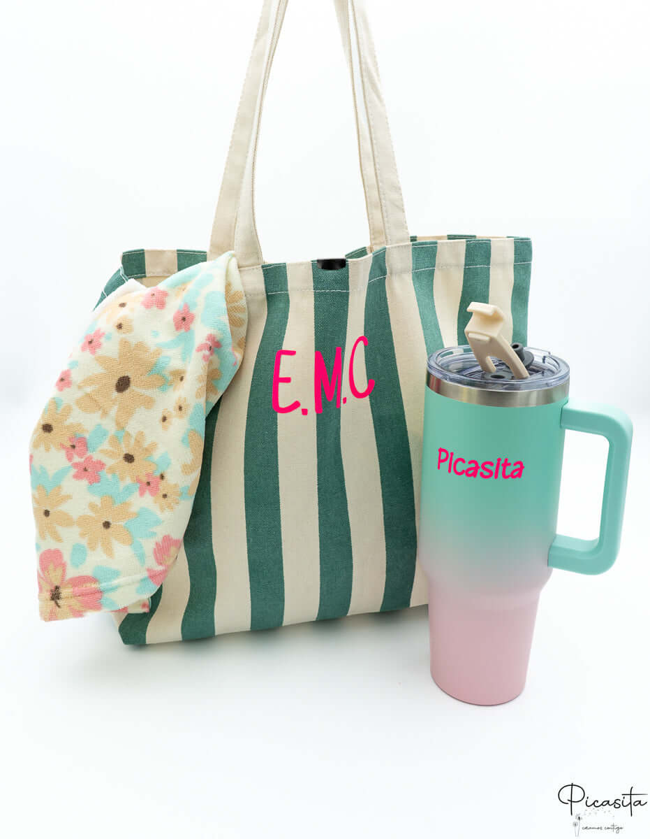 Bolso de playa verde junto a una botella térmica y una toalla con estampado floral.
