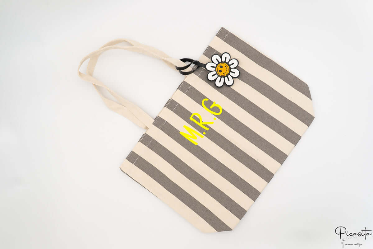 Bolso para piscina con rayas grises y blancas decorado con un charm de margarita.